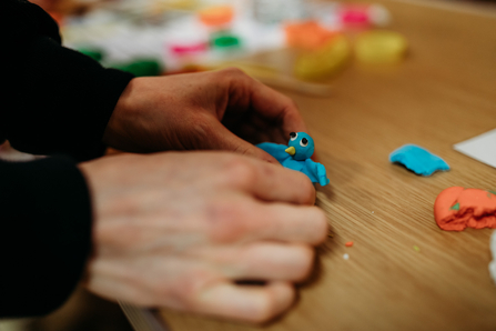 An image of some hands making a blue bird out of modelling clay. 