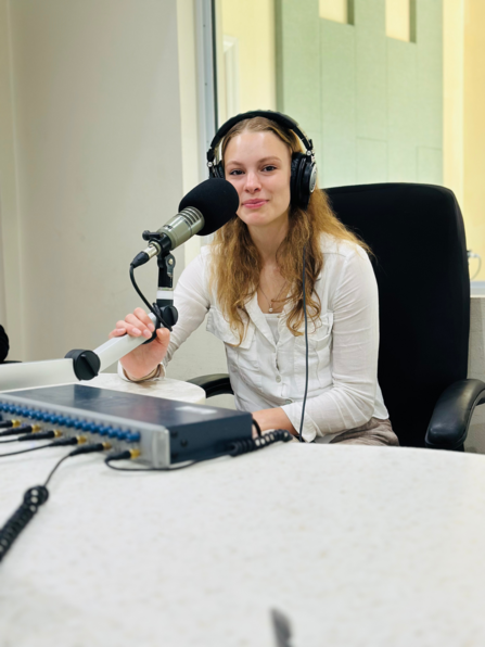 Blonde woman with headset on sitting in front of a microphone