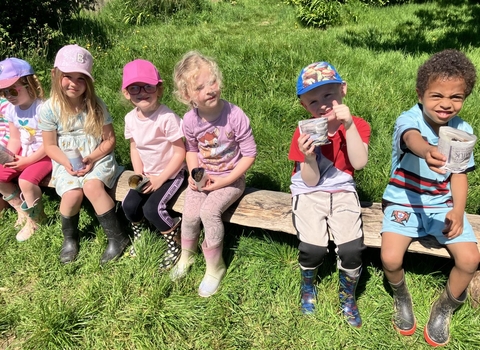 Children sat on a bench holding newspaper plant pots